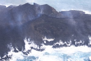 写真 6. 火砕丘西側から流出している溶岩流．溶岩先端部では，高温の溶岩と海水との接触により蒸発した海水が激しく立ち昇っている．西から撮影．