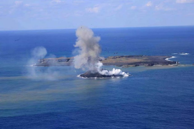 写真１。西之島と新島の噴火活動の遠景。11 月24 日昼前。 海に達した溶岩流の先端からは水蒸気の白煙が上がる。同じく南東側から撮 影。 