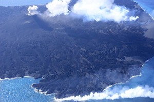 写真１：東側から見た西之島。左上にある中央火砕丘ではストロンボリ式噴火を繰り返しており，その裾野から樹枝状の溶岩流が四方に広がる。東側では溶岩が海に注いでいる。