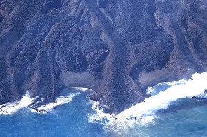 写真２：東側で海に注ぐ溶岩流。溶岩堤防に囲まれた新鮮でごつごつした表面の溶岩が海中に没し，水蒸気を上げている。